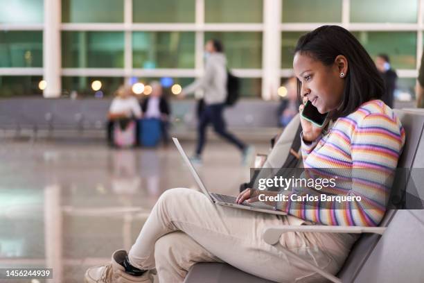 woman telecommuting from the airpot, sitting in the boarding room using laptop and speaking on the phone. - airport hipster travel stockfoto's en -beelden