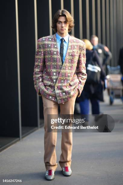 Guest wears a black shiny leather tie, a pale blue shirt, a beige and brown with yellow and pink embroidered checkered print pattern nailed /studded...