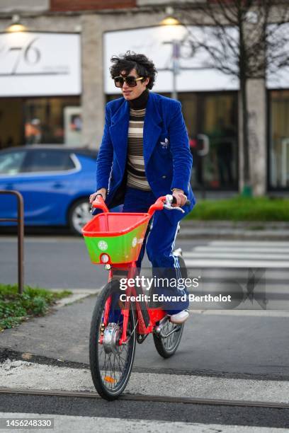 Guest wears black square sunglasses, a black / gray / white striped print pattern wool pullover, a royal blue velvet blazer jacket from Gucci x...