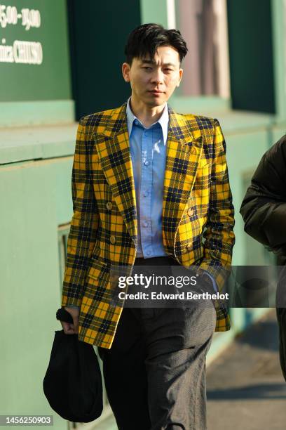 Guest wears a pale blue shirt, a yellow and black checkered print pattern blazer jacket, dark gray large suit pants, a black ribbed handbag, outside...