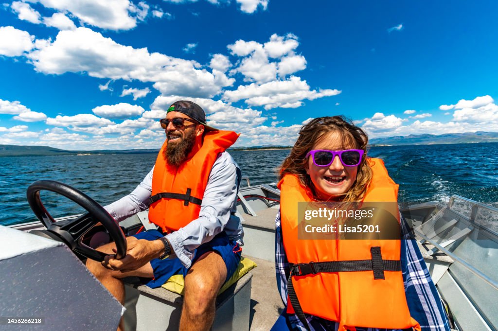 Happy father and daughter wearing life jackets on a small motor boat on a scenic lake with his family, togetherness in nature