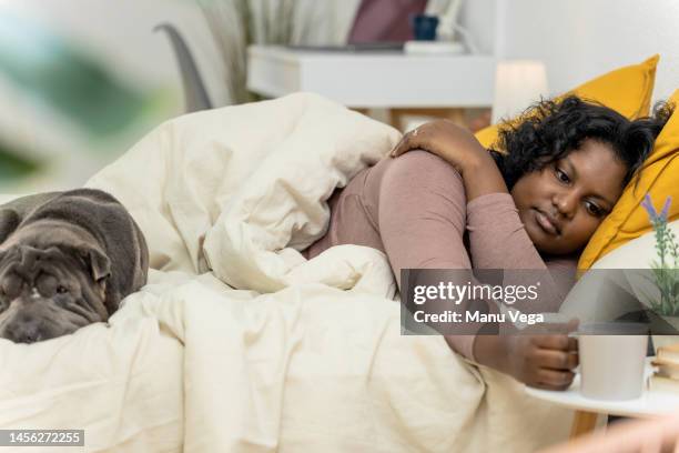 woman grabbing a cup of coffee while waking up in bed with her dog. - monday fotografías e imágenes de stock