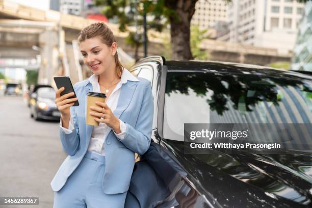 successful smiling attractive woman in formal smart wear is using her smart phone while standing near modern car - formal office stock pictures, royalty-free photos & images