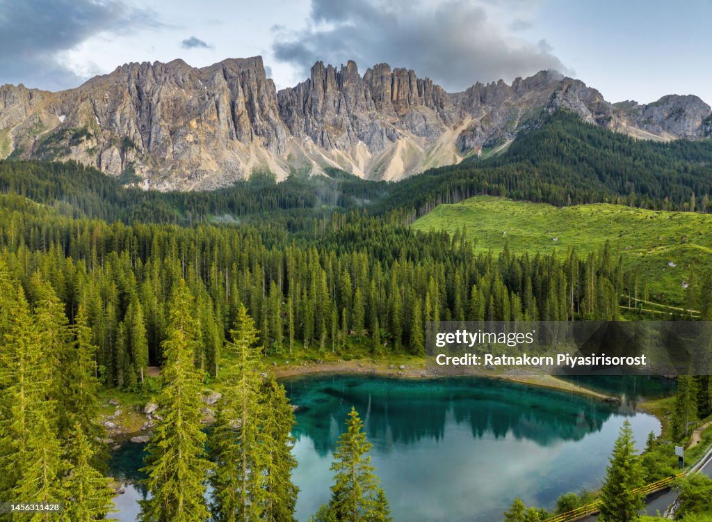 Aerial Drone Sunset Scene of Italian alps. Silent morning on the lake of Carezza surrounded by pine forest and mountains.