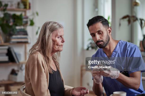 male nurse explaining glaucometer to senior woman at home - nurse with old male patient home care stock-fotos und bilder