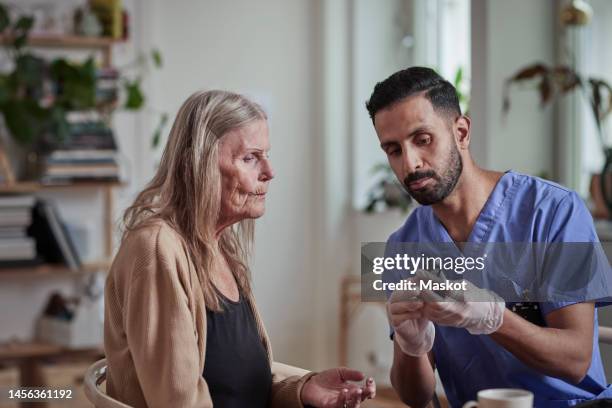 male nurse explaining glaucometer to senior woman at home - diabetes care stock pictures, royalty-free photos & images