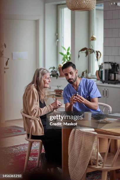 senior woman and nurse discussing over glaucometer while sitting on chair at home - glaucometer stock pictures, royalty-free photos & images