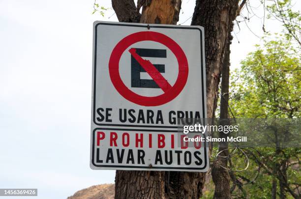 spanish-language sign indicating 'no estacionamiento. se usara grua. prohibido lavar autos' [no parking. tow truck will be used. no car washing] attached to a tree - placa de proibido estacionar imagens e fotografias de stock