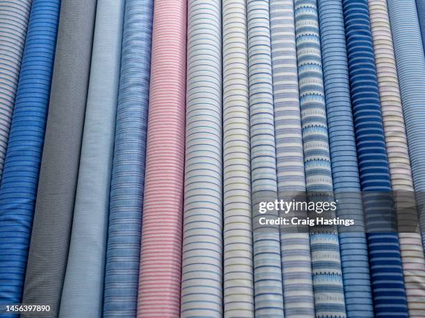 rolls of multi coloured professional looking fabric found in a tailors shop for making custom suits, dresses and shirts - rolled up stock pictures, royalty-free photos & images