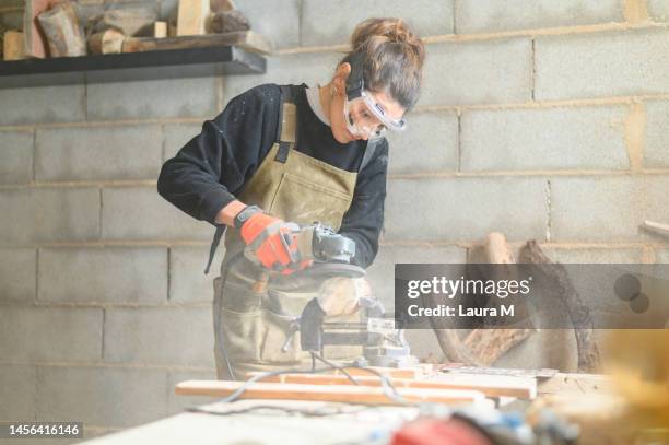 職場で機械で木を磨く若い大工の女性。職場でポリッシャーと一緒に働く眼鏡をかけた若い大工の女性。 - wood worker posing ストックフォトと画像