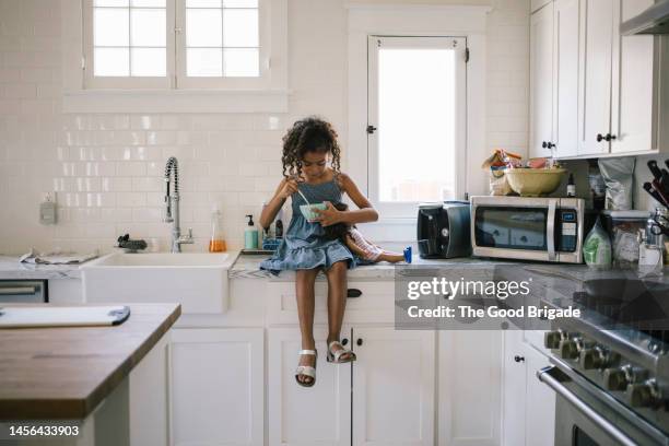girl having breakfast while sitting on kitchen counter at home - microwave photos et images de collection