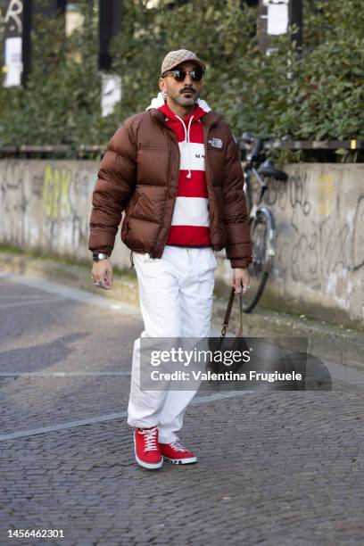 Guest is seen wearing a The North Face puffer jacket, a Sunnei striped sweater, Gucci baseball hat, red sneakers and white pants outside the MSGM...