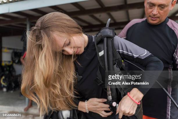 el hombre maduro ayuda a una mujer joven a ajustar el equipo submarino y el aqualung antes del viaje de buceo. - aqualung diving equipment fotografías e imágenes de stock