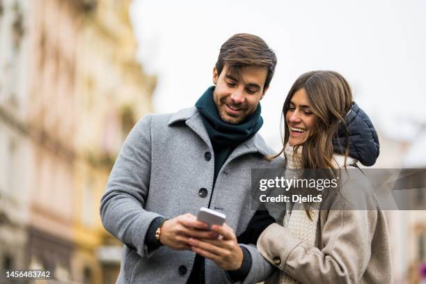 young couple using smart phone in the city. - winter woman showing stock pictures, royalty-free photos & images