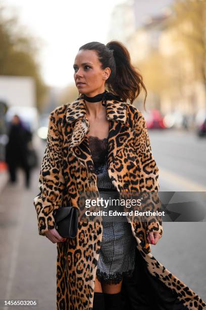 Guest wears a silver large cross pendant earring, a black ribbon necklace, a camel / brown / black leopard print pattern fluffy long coat, a black...
