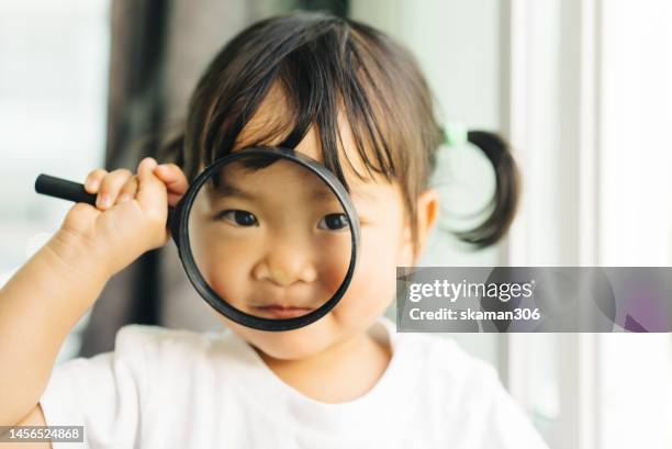 positive emotion asian toddler enjoy playing with magnifying glass  at home weekend activity - see through ストックフォトと画像