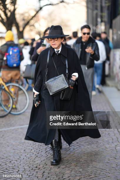 Guest wears a black felt / wool hat, black glasses, a white shirt, a black tie, a black oversized long cloak coat, a black shiny leather borders and...