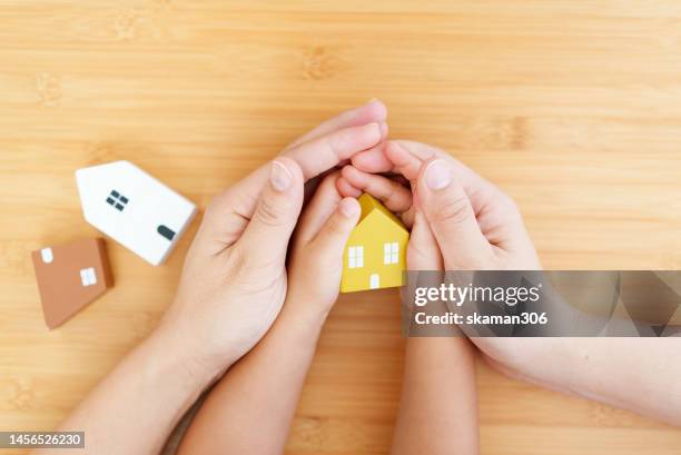 hand mother and daughter holding a small wooden house together on bamboo background concept family and home loan - wohngebäudeversicherung stock-fotos und bilder