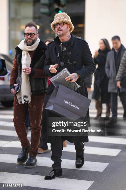 Guest wears a beige fluffy bob hat, black glasses, a black t-shirt, a black shiny leather with embroidered nailed / studded jacket, a black long...