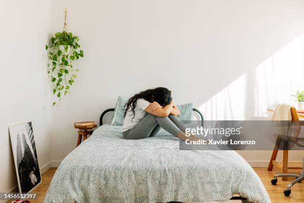 lonely young woman feeling depressed sitting head in hands on bed. sad teenage girl crying on bedroom feeling stressed. negative emotion and mental health concept - avoids fotografías e imágenes de stock