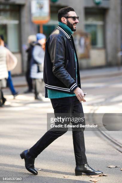 Guest wears black sunglasses, a green wool ribbed turtleneck pullover, a black shiny leather bomber coat, black denim pants, black shiny leather...