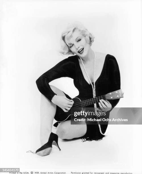 Marilyn Monroe sitting wearing a long pearl necklace and playing the ukulele in a scene from the film 'Some Like It Hot', 1959.