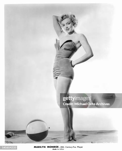 Marilyn Monroe standing in a one piece bathing suit with a beach ball at her feet circa 1952.