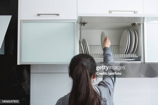 young girl picking up the dishes kitchen in cupboard. - cabinet door stock pictures, royalty-free photos & images