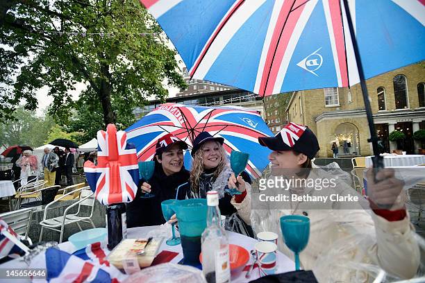 Tatjana Naidea, Elena Volkova and Diana Kelso from Russia, shelter from the rain at the Kings road street party on June 3, 2012 in London, England....