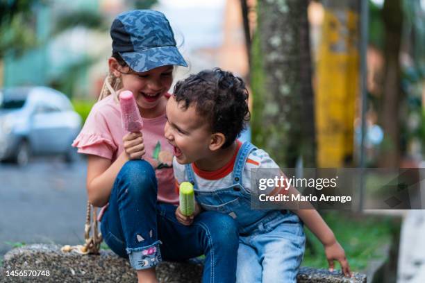 zwei kleine brüder essen gerne ihr eis am stiel, während sie auf der straße spielen - girl eating messy ice cream cone stock-fotos und bilder