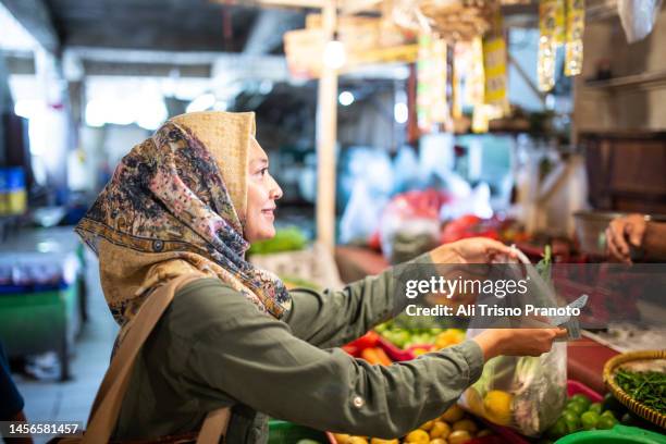 beautiful hijab woman is shopping in traditional market, paying with cash - java note stock pictures, royalty-free photos & images