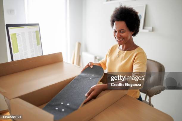 mid adult black woman shopaholic customer sitting and unpack parcel - skateboard shop stock pictures, royalty-free photos & images