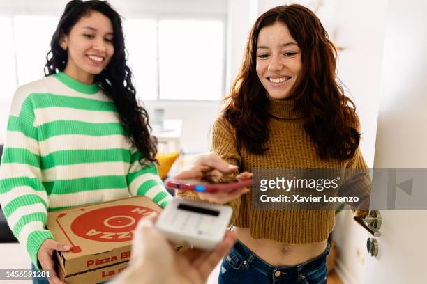 young woman using mobile phone app to pay food delivery on wireless terminal. customer paying for pizza with smartphone at home - pizza delivery stock-fotos und bilder