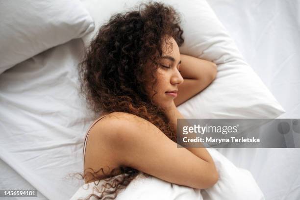a black woman lies in bed. white linens. dream. cheerful morning. good dream. soft bed. orthopedic mattress. - one young woman only photos et images de collection