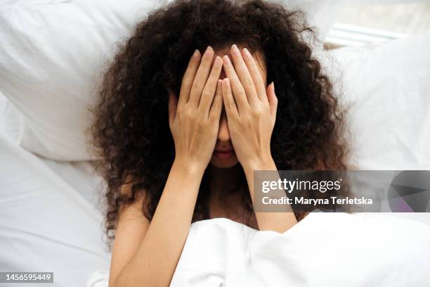 a dark-skinned woman lies in bed and covers her face with her hands. black girl in bed. heavy morning. reluctance to wake up and go to work. bad dream. sleeplessness. - woman face close up stock pictures, royalty-free photos & images