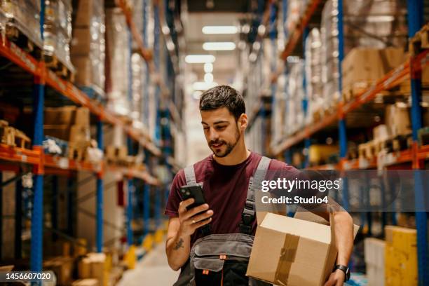 trabajador de almacén enviando mensajes de texto por teléfono - trabajador de almacén fotografías e imágenes de stock