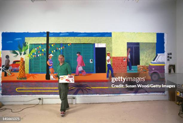 English artist David Hockney poses in front of a large painting of a street scene in his studio, 1980.