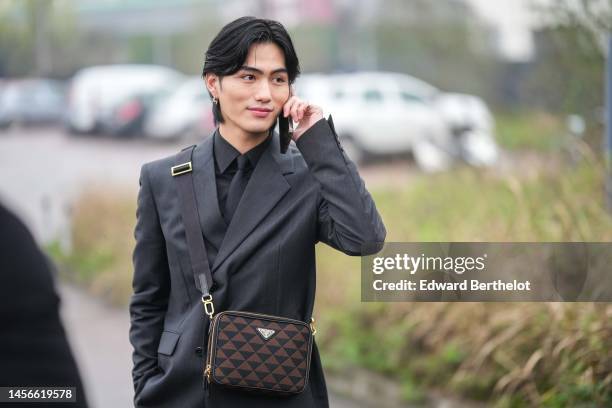 Guest wears silver earrings, a black shirt, a black tie, a dark gray blazer jacket, a black and brown triangular print pattern crossbody bag from...