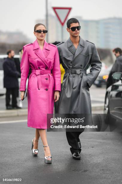Guest wears black sunglasses, a neon pink shiny leather long belted coat from Prada, a silver shiny varnished leather heels sandals, a guest wears...