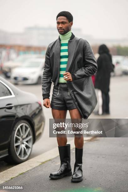 Guest wears silver earrings, a pale green and green striped print pattern wool / turtleneck pullover, a black shiny leather bomber coat from Prada, a...
