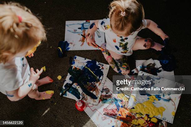 twin girls create a huge mess with primary coloured paints - baby paint stock-fotos und bilder
