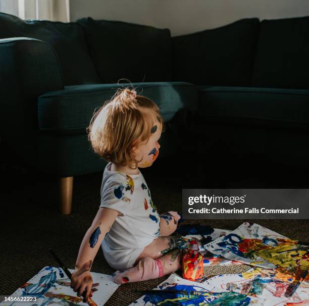 a toddler girl creates a huge mess with primary coloured paints - kids mess carpet fotografías e imágenes de stock