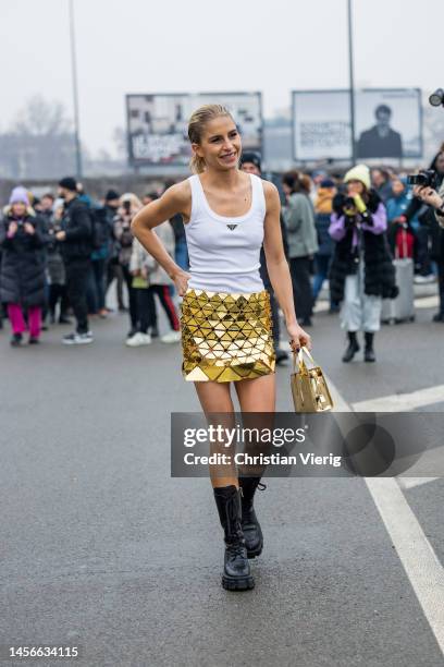 Caroline Caro Daur wears white top with logo, golden skirt, bag, black laced boots outside Prada during the Milan Menswear Fall/Winter 2023/2024 on...