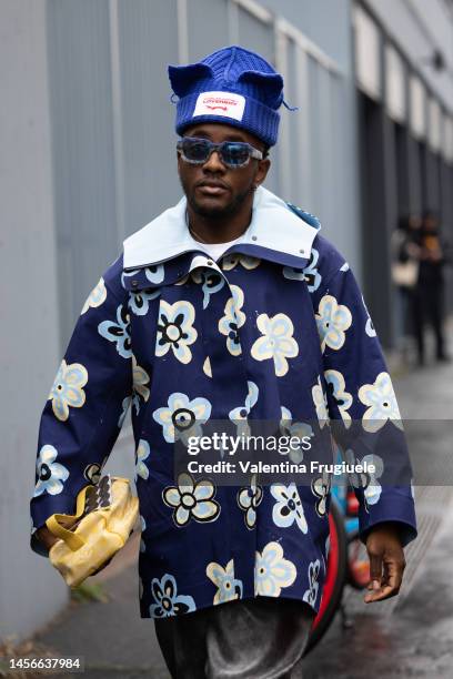 Guest is seen wearing a Charles Jeffrey Loverboy blue ribbed beanie, printed flower jacket, silver pants and yellow bag outside the Magliano show...