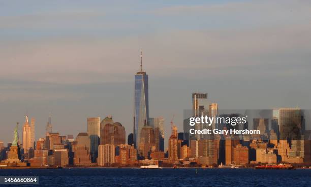 The sun sets on the Statue of Liberty, the Empire State Building and the skyline of lower Manhattan and One World Trade Center in New York City on...