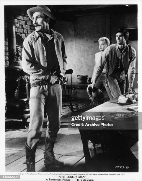 Jack Palance putting on his belt as Elaine Aiken and Anthony Perkins move towards sound they hear in a scene from the film 'The Lonely Man', 1957.