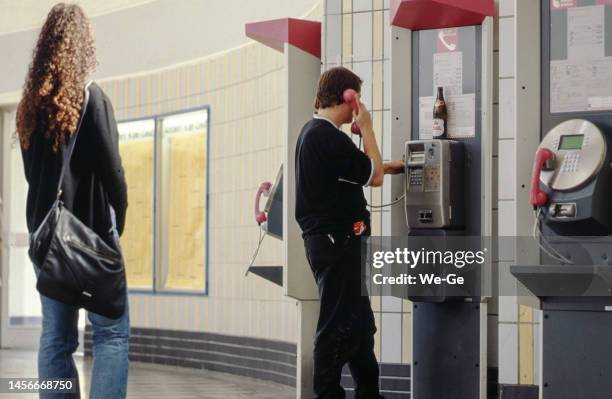 historic image of a young man making a phone call at a pay phone at cologne deutz station, a young lady waits for him to finish. - pay phone stock pictures, royalty-free photos & images