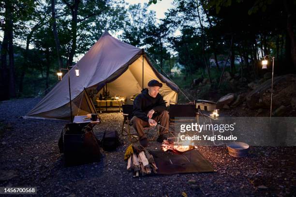 asian man roasting marshmallows over a campfire flame. - only japanese stock-fotos und bilder