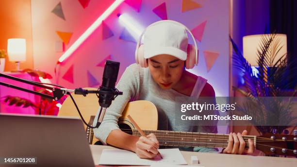 happy asian girl influencer wear headphone record podcast on laptop play guitar writing notes to music book onair online live streaming at studio room. - singer songwriter stockfoto's en -beelden