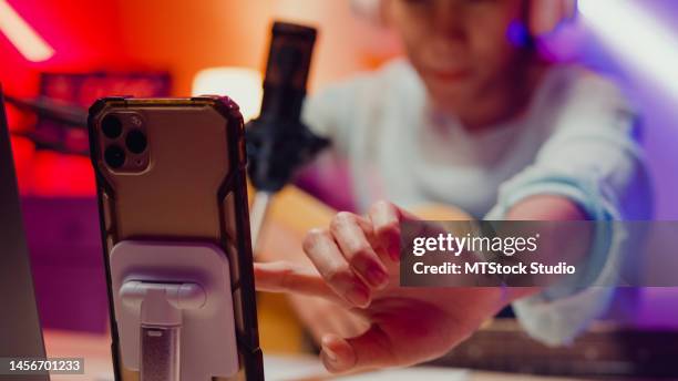 close-up happy asian girl influencer indossare cuffie con chitarra registrare podcast onair online live streaming talk follower comment e pubblico al telefono in studio di casa. - content foto e immagini stock